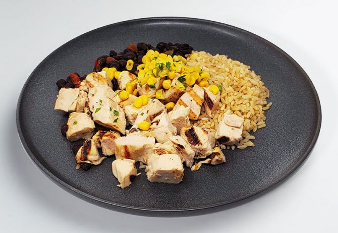 A plate containing grilled chicken breast pieces, brown rice, black beans, and roasted corn.MEAL PREP BY SPARTAN MEAL PREPS MIAMI