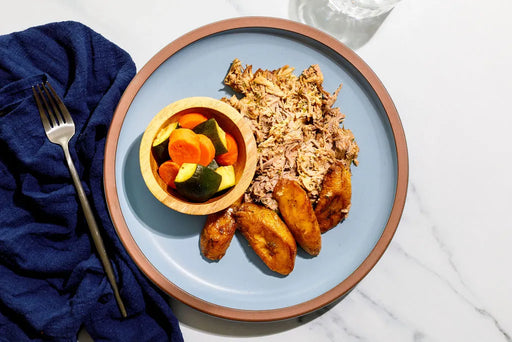 Plate of food with rice, plantains, and vegetables on a blue plate with a fork.