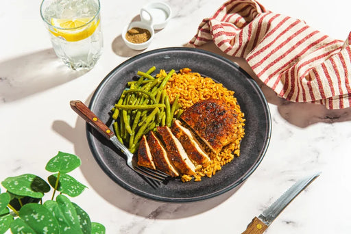 Dish with rice, green beans, and sliced meat on a white tablecloth with a glass of water and lemon.