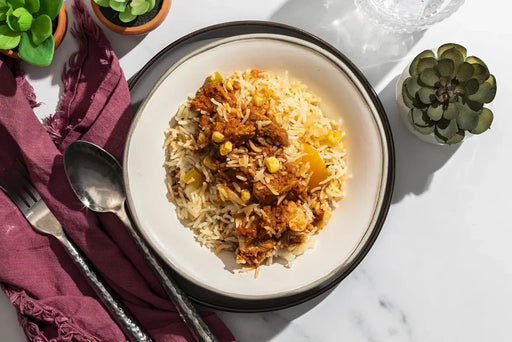 Bowl of fried rice with chicken on a marble surface with a purple napkin and silver spoon.
