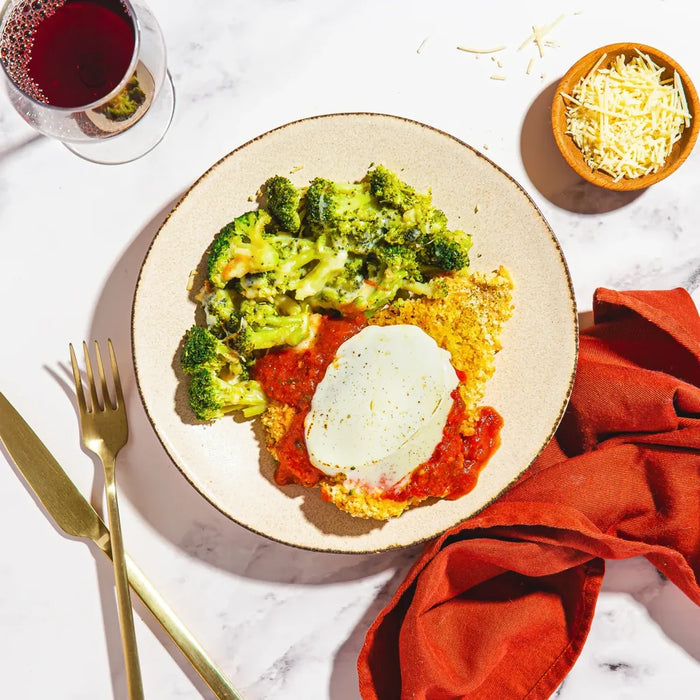 Plate of food with broccoli, cheese, and a red sauce on a marble surface with a glass of red wine.