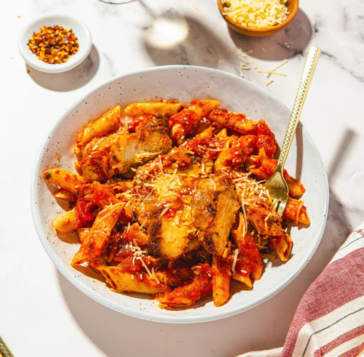 Penne pasta with tomato sauce in a white bowl on a light surface.