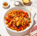 Penne pasta with tomato sauce in a white bowl on a light surface.