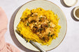 Plate of yellow spaghetti with mushrooms and herbs on a light background