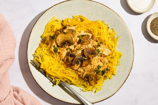 Plate of yellow spaghetti with mushrooms and herbs on a light background