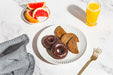 Assorted donuts on a plate with a glass of orange juice and grapefruit slices on a marble surface.