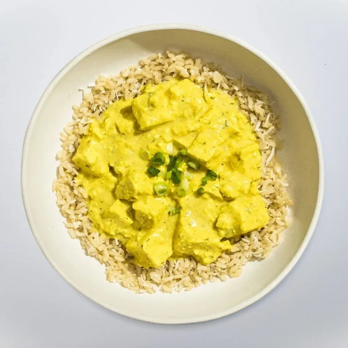 Yellow curry over brown rice on a white plate with a light gray background