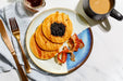 Plate of pancakes with syrup, bacon, and coffee on a white tablecloth.