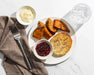 Plate of roasted sweet potatoes, a biscuit, and a small bowl of jelly on a marble surface with a fork and napkin.