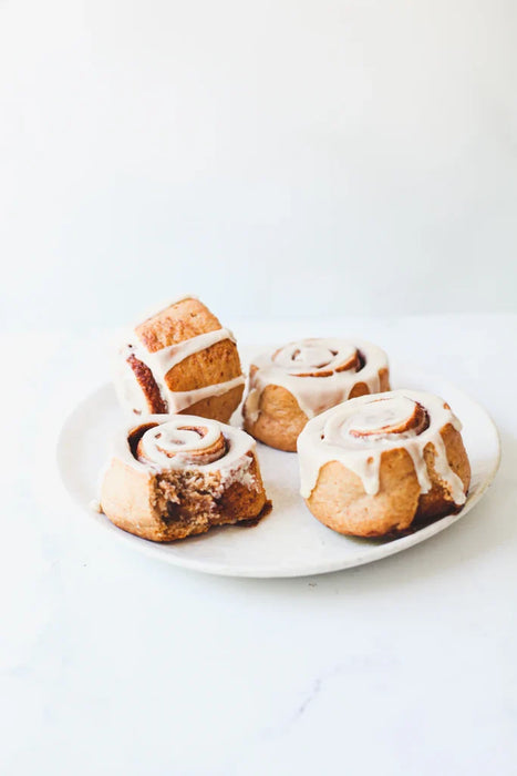 Four cinnamon rolls with icing on a white plate against a light background
