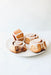 Four cinnamon rolls with icing on a white plate against a light background