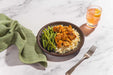 Bowl of food with green beans and rice on a marble surface with a glass of orange juice.