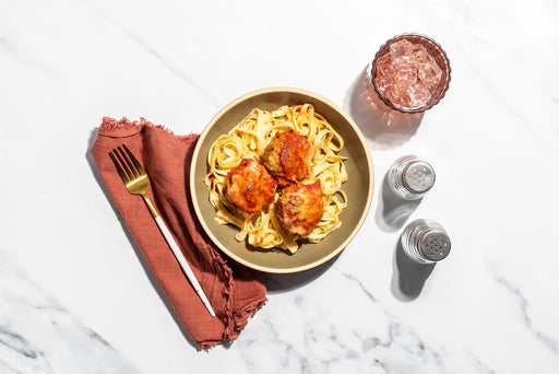 Plate of pasta with meatballs on a marble surface with a glass of water.