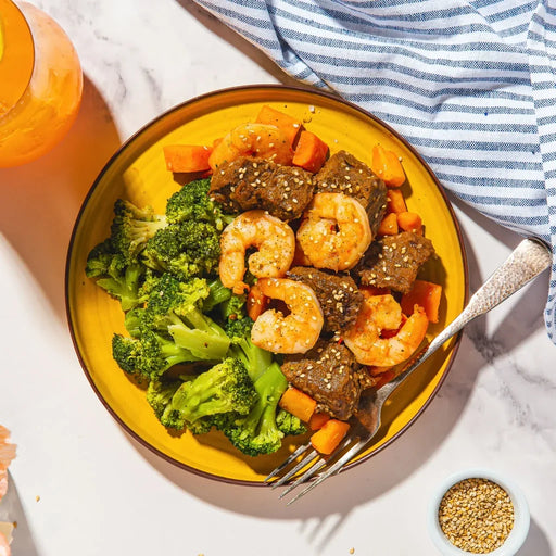 Yellow plate with shrimp, broccoli, and carrots on a marble surface