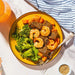 Yellow plate with shrimp, broccoli, and carrots on a marble surface