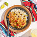 Plated dish of rice and vegetable curry with a colorful napkin and lime wedges on a white surface.
