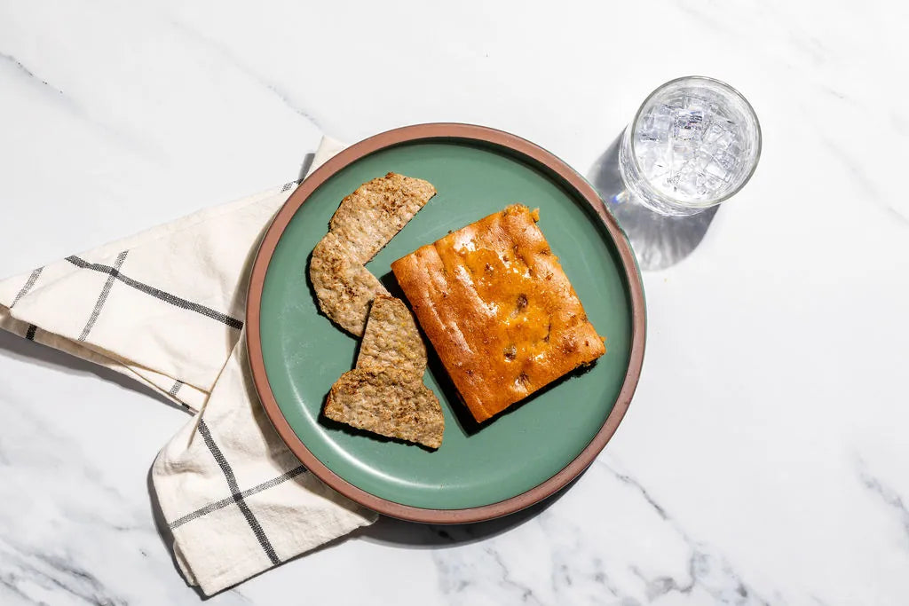 Two pieces of bread on a green plate with a glass of water on a marble surface.