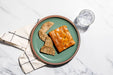 Two pieces of bread on a green plate with a glass of water on a marble surface.