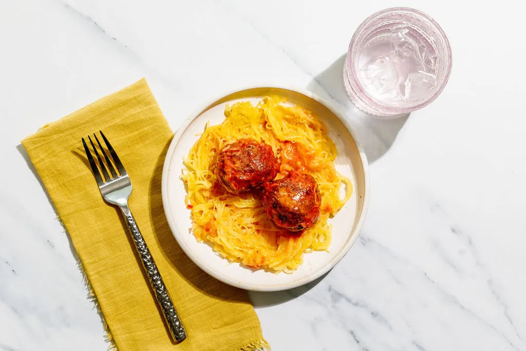 Plate of pasta with meatballs on a marble surface with a yellow napkin and fork.