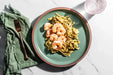 Green plate with shrimp and pasta on a marble surface with a green napkin and fork.