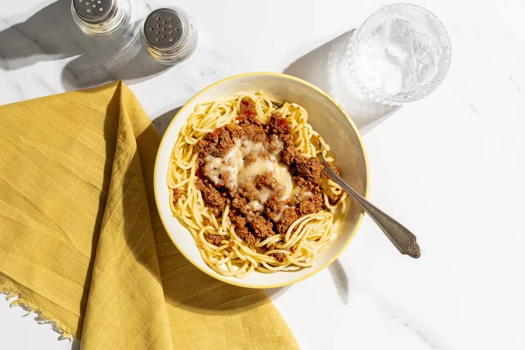 Bowl of spaghetti with meat sauce on a white tablecloth with a yellow napkin.
