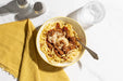 Bowl of spaghetti with meat sauce on a white tablecloth with a yellow napkin.