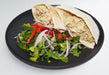 Pita bread stuffed with a salad on a black plate. A meal made by spartan meal preps miami.