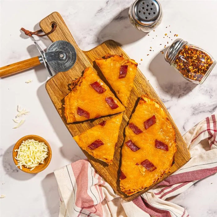 Wooden cutting board with pizza slices, cheese, and pepper shakers on a marble surface.