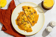 Omelette with sausage and vegetables on a plate with a side of orange juice.
