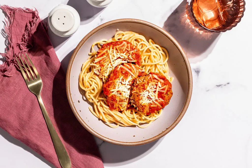 Plate of spaghetti with tomato sauce and cheese on a marble surface with a pink cloth and candle.