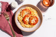 Plate of spaghetti with tomato sauce and cheese on a marble surface with a pink cloth and candle.