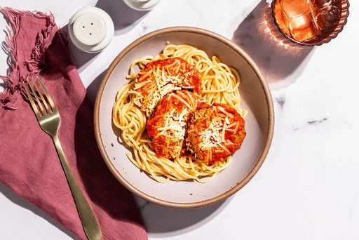 Plate of spaghetti with tomato sauce and cheese on a marble surface with a pink cloth and candle.