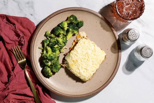 Plate of food with broccoli and a piece of bread on a marble surface.