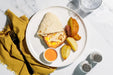 Plate with a wrap, sweet potato, and apples on a marble surface with a yellow napkin and fork.