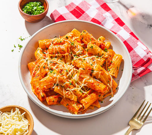 Pasta dish with red sauce and cheese in a white bowl on a checkered cloth.