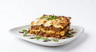 Slice of lasagna on a white plate with a white background