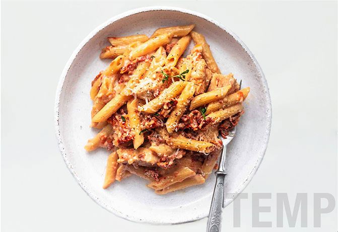 Plate of penne pasta with sauce on a white background