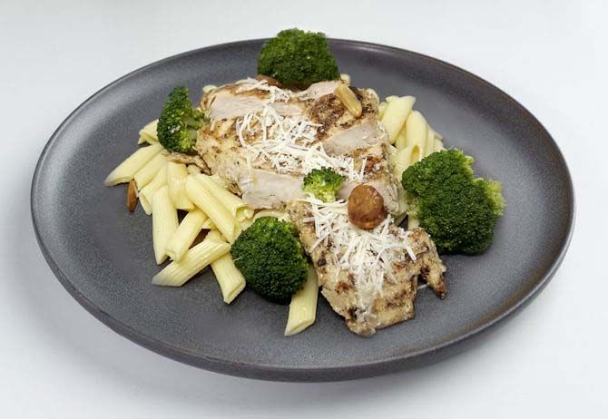 A plate of Roma Grilled Chicken Pasta with penne pasta, flame grilled chicken, roasted broccoli, and shaved Parmigiano Reggiano.
